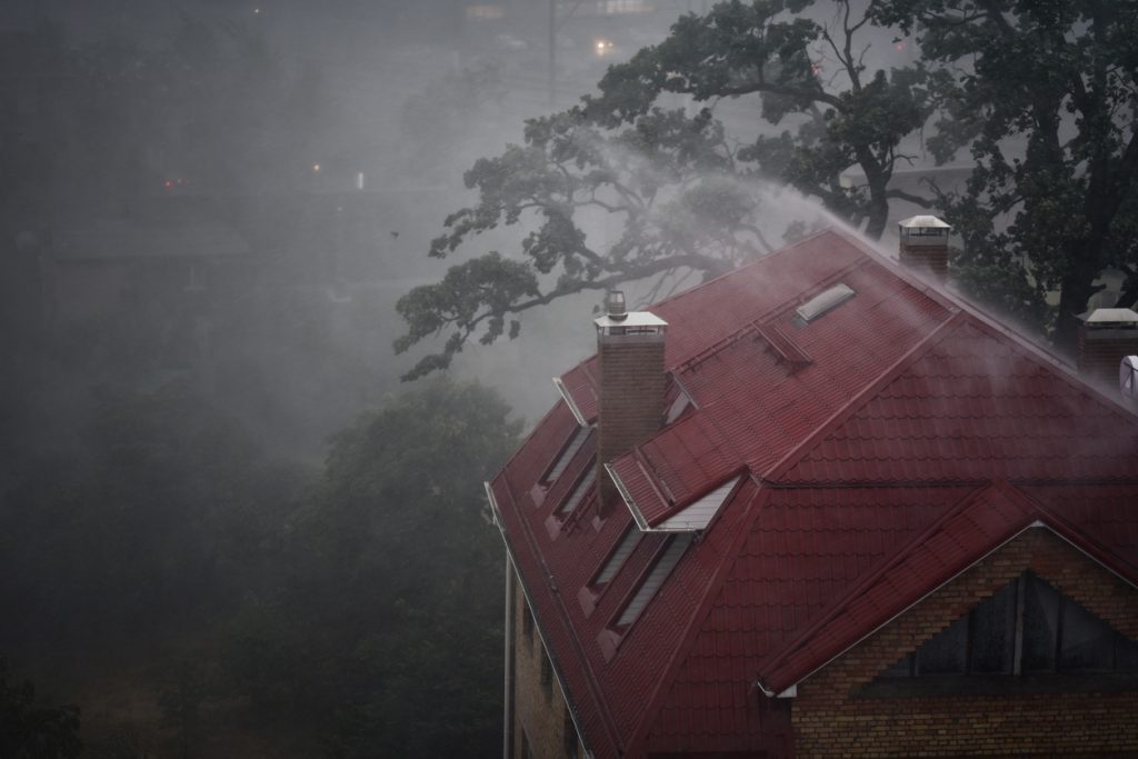 An image of heavy rain beating down on the roof of a large home with a red roof