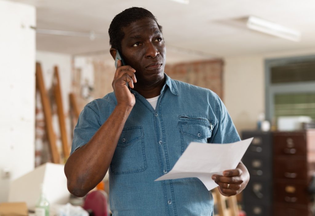 Concerned man on phone holding paperwork and discussing a denied hurricane insurance claim.