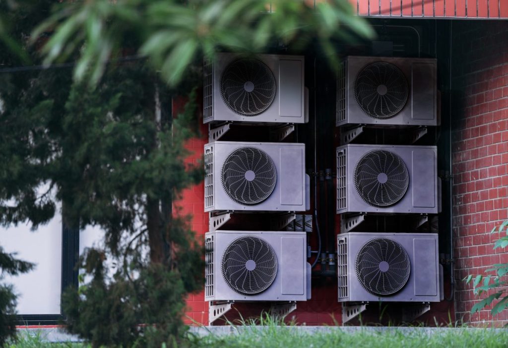 Outdoor HVAC units covered in soot and residue, partially obscured by trees, illustrating hidden contamination often overlooked in denied smoke damage insurance claims.