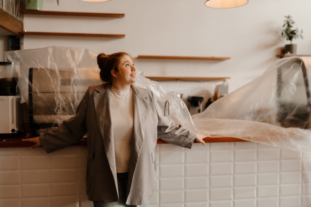 Small business owner standing inside a café under renovation with equipment covered in plastic, symbolizing how extra expense coverage helps businesses recover and continue operating after unexpected disruptions.
