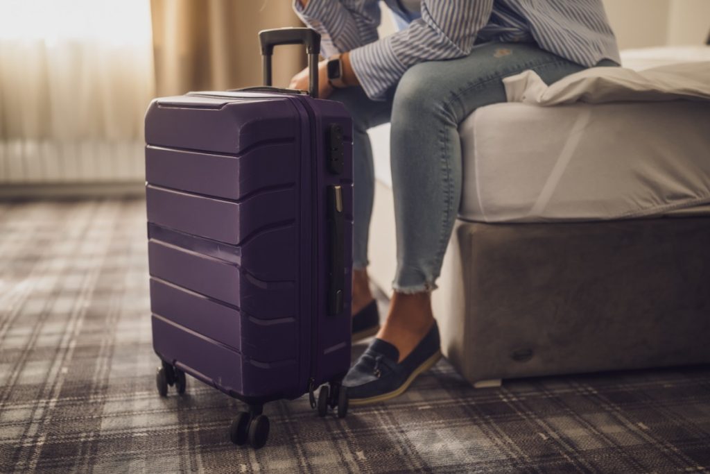 Person sitting on a bed with a packed suitcase, symbolizing temporary relocation expenses covered under loss of use coverage after a home becomes uninhabitable.