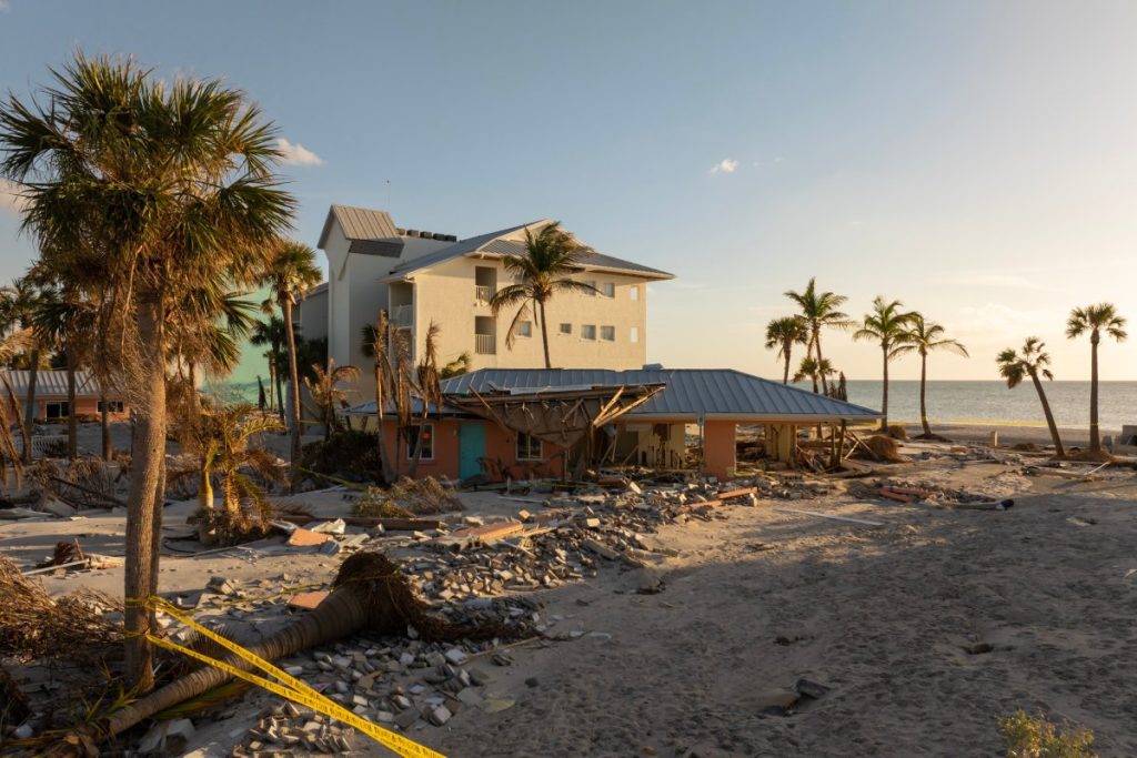 A beachfront property in Florida shows severe storm surge damage with fallen palm trees, debris, and destroyed buildings, illustrating the importance of having Florida flood insurance after hurricanes.